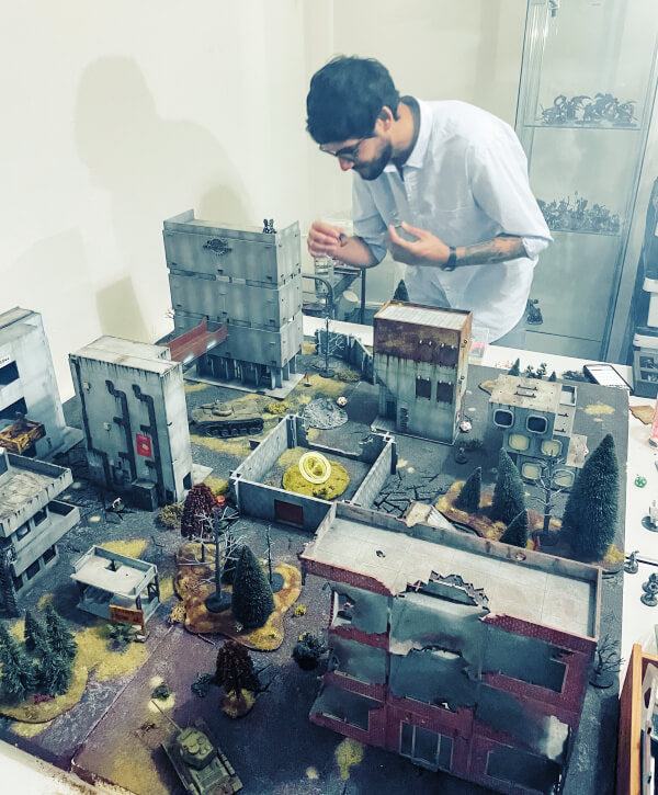 Tabletop wargaming game with terrain buildings and man moving a miniature
