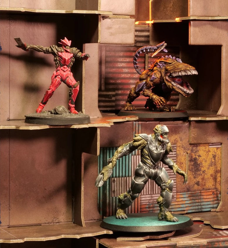 Three painted tabletop gaming miniatures displayed on a rustic brown shelf-like terrain: a red armored figure on the left, a large brown reptile-like monster on the upper right, and a silver-green armored figure on a teal base on the lower right.