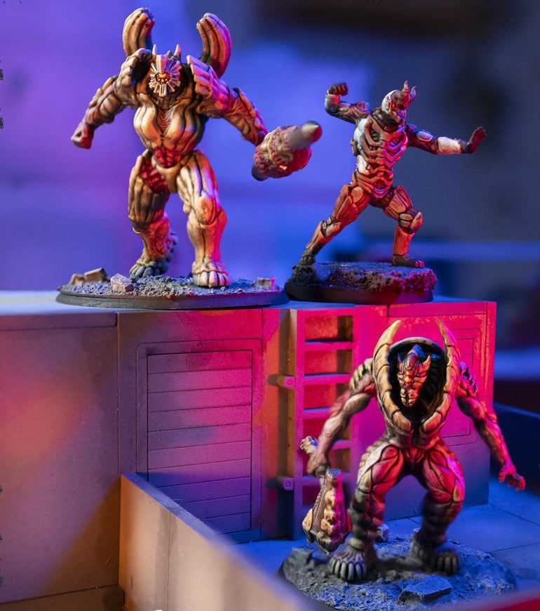 Three painted sci-fi monster miniatures displayed on a tabletop gaming diorama with purple and pink lighting.
