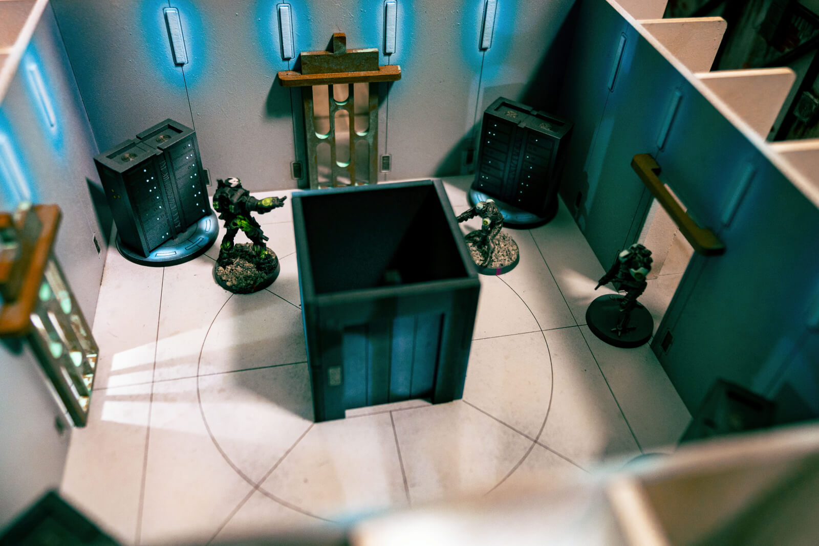 Infinity miniatures inside an objective room terrain building with blue lights and central lift core.